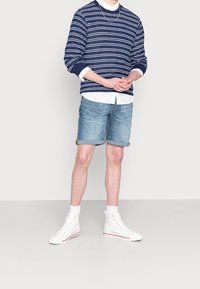 Navy-strippowany sweter z białymi akcentami, jasnoniebieskie szorty dżinsowe i białe sneakersy za kostkę. Nałożony z białą koszulą pod spodem.