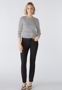 Zwarte skinny jeans met vijf zakken en knoopsluiting, gecombineerd met een zwart-wit gestreept langslief top met een brede halslijn.