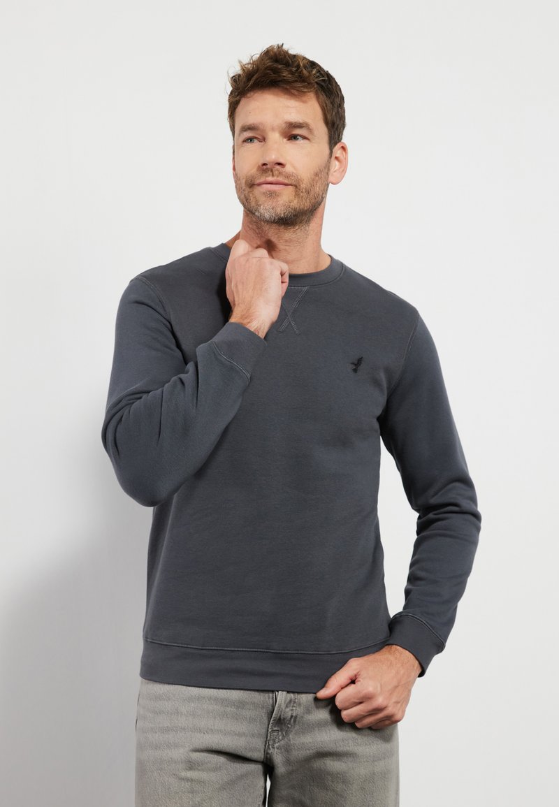 Sudadera gris oscuro con cuello redondo, mangas largas y un pequeño logo en el pecho. Textura suave con puños y dobladillo acanalados.