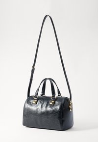 Sac à main synthétique noir texturé avec quincaillerie dorée. Dispose de poignées courtes et d'une bandoulière détachable. Forme ronde avec des accents de clous.