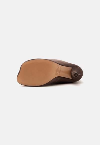 Chaussure à semelle en cuir marron vue par le dessous, montrant une semelle lisse et un détail circulaire cousu près du talon.