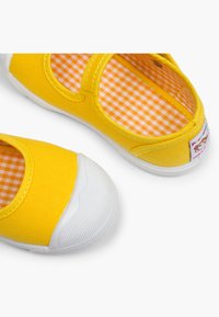 Zapatos de lona amarillos con una puntera de goma blanca y un interior de estampado de cuadros. Presentan una correa de gancho y bucle para un ajuste seguro.