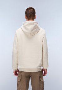 Sudadera color crema en una tela suave, con un bolsillo tipo canguro, puños acanalados y capucha con cordón, combinada con pantalones cargo beige.