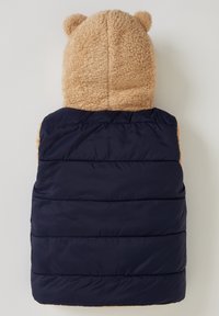 Beige Teddyfellkapuze mit Bärenohren, die an einer marineblauen, gepolsterten Weste mit horizontalen Nähten befestigt ist. Das Material kombiniert plüschige und glatte Texturen.