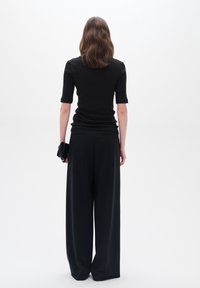 Svart ribbad topp med korta ärmar, tillsammans med löst sittande svarta vida byxor. Modellen håller en liten svart clutch.