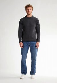 Pull en maille gris foncé avec un col rond et un ourlet côtelé, associé à un jean bleu à jambes droites et des baskets blanches.