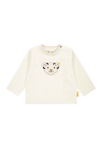 Cremfarbendes Langarmshirt mit einem gestickten Löwenkopfmuster auf der Vorderseite, das subtile gelbe und schwarze Details sowie ein Seitenetikett aufweist.
