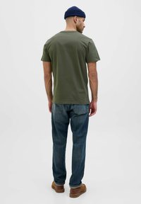 T-shirt in cotone verde oliva con maniche corte, scollo rotondo, design aderente. Indossato con jeans in denim blu e scarpe marroni. Stile semplice e basic.
