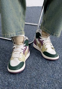 Osoba s zelenim, bež i ljubičastim visokim tenisicama s bijelim vezicama i plavim trapericama sjedi na stolici s metalnom nogom.