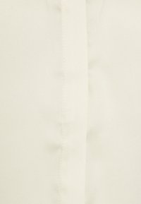 Ljus krämfärgad tyg med en slät textur som har diagonala vävningsmönster och en vertikal söm. Ingen synlig hårdvara eller dekorationer.