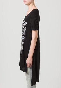 Černá tunika s krátkým rukávem a výstřihem do V, zdobená květinovým vzorem v modrých a šedých odstínech, mírně delší vzadu. Měkká látka.