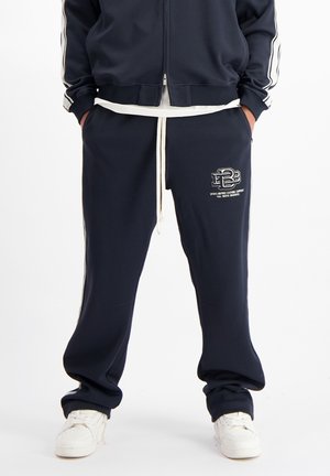 Marineblauwe sweatpants met witte zijstrepen, elastische taille met trekkoord en logo-detail. Gemaakt van zachte stof, met een relaxte pasvorm en minimalistisch ontwerp.
