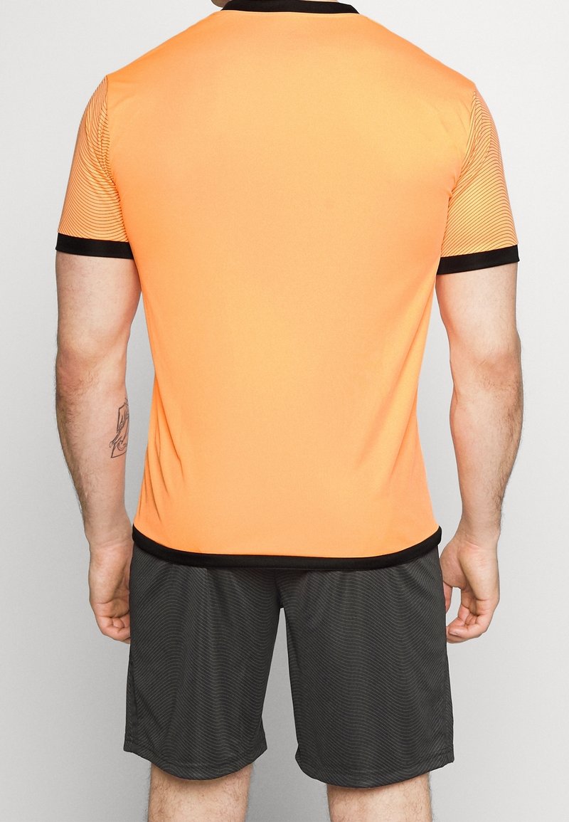 Orange idrottströja med svarta detaljer och korta ärmar, med en slät textur. Tillsammans med svarta randiga shorts, vilket skapar en enhetlig look.