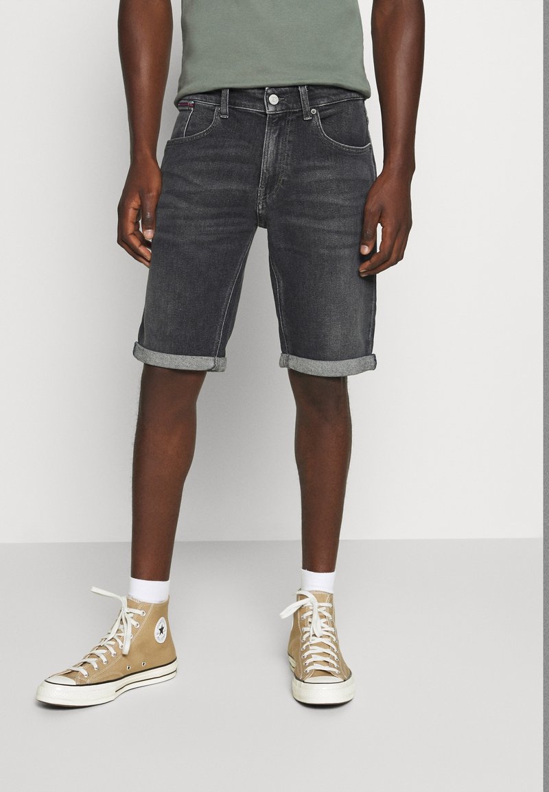 Tummansiniset farkkuhousut lyhyinä, käännetyt lahkeet, yhdistettynä vihreään paitaan ja beigeihin korkeisiin tennareihin, joissa on valkoiset nauhat ja kumipohjat.