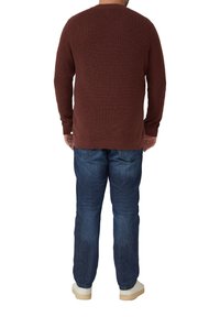 Brązowy prążkowany sweter z dzianiny z długimi rękawami, zestawiony z wyblakłymi niebieskimi dżinsami i jasnymi trampkami, widziany od tyłu.