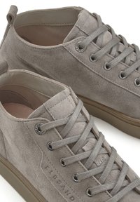 Light gray suede sneakers with rounded toe, flat laces, and metal eyelets. Rubber sole and subtle branding on the side. Smooth interior lining.