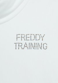 T-shirt bianco in cotone con la scritta "FREDDY TRAINING" in paillettes argento e oro. Collo rotondo, texture liscia, design semplice.