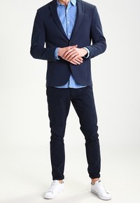 Námořnický blejzr přes světle modrou pruhovanou košili, doplněný tmavými kalhotami a bílými teniskami. Jednoduchý design a přizpůsobený střih.