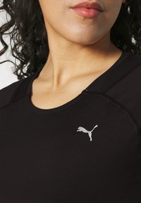 Černé sportovní tričko s kulatým výstřihem, hladkým povrchem a výrazným stříbrným logem Puma na levé části hrudi. Viditelně zesílené švy.