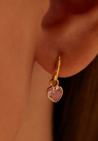 Goldene Creolen mit einem herzförmigen, pinkfarbenen Edelsteinanhänger, der eine polierte Oberfläche und ein einfaches, elegantes Design aufweist.