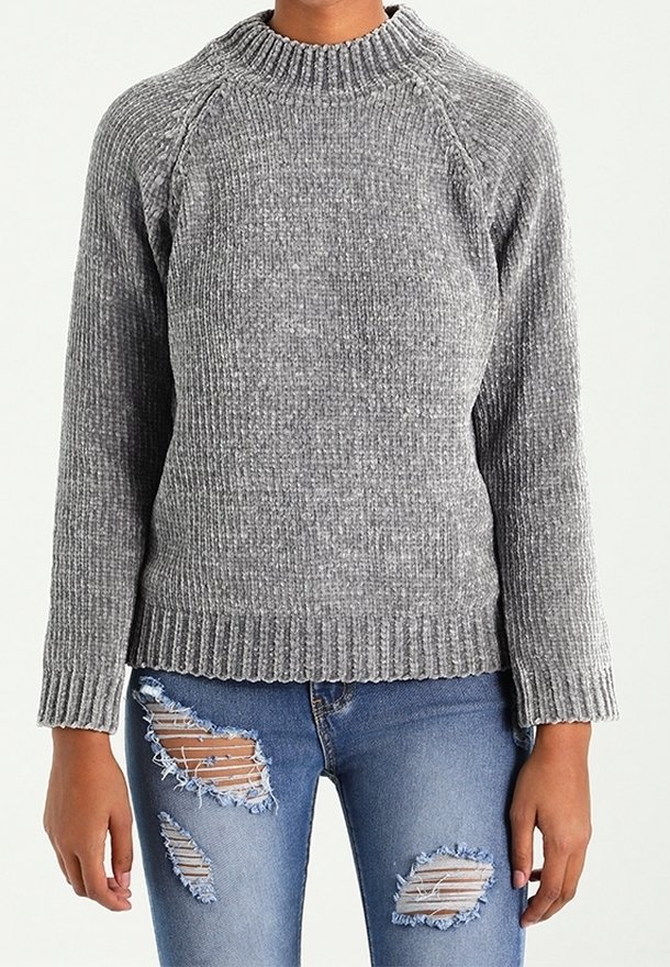 Grauer gerippter Strickpullover mit hohem Kragen und Raglanärmeln, kombiniert mit zerrissenen blauen Jeans, die mehrere Risse und ausgefranste Säume aufweisen.