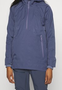 Granatowa wodoodporna kurtka z zamkiem z przodu, bocznymi kieszeniami i kapturem. Gładka tekstura, minimalistyczny design i subtelne logo.