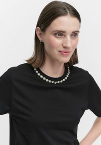 Svart T-shirt med rund halsringning dekorerad med små, blommiga utsmyckningar. Slät textur och korta ärmar.