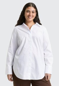 Wit overhemd met lange mouwen en een button-down kraag, voorzien van een subtiel gestipeld patroon. De stof oogt glad met een ontspannen pasvorm.