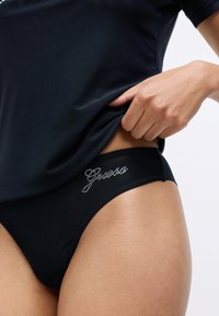 Fekete bikinialsó, rugalmas derékpánttal, textúrált anyaggal és kristály díszítésekkel, amelyek egy ívelt márkanevet formáznak.