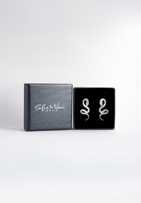 Orecchini a forma di serpente in argento, esposti su un supporto in velluto nero, presentati in una scatola nera strutturata con scritte bianche.