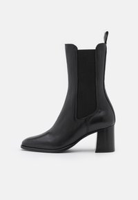 Bottine en cuir noir avec pans latéraux élastiques, bout pointu et talon épais. Texture lisse avec peu de détails.