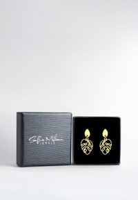 Örhängen i guldbladform visade i en svart sammetfodrad låda med en texturerad silveryta och logotypinskription på locket.
