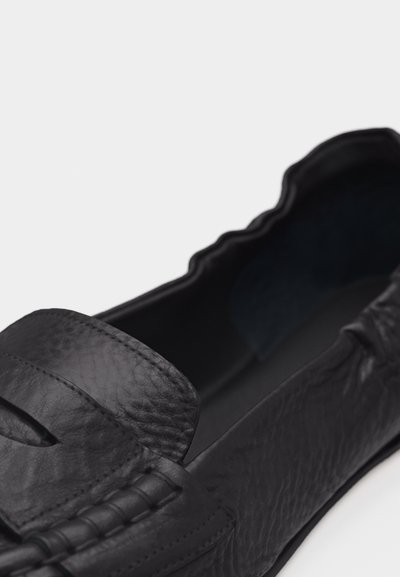 Mocassin en cuir noir avec une finition texturée et une bande cousue de style mocassin sur le dessus.