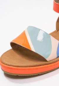 Sandale à bout ouvert avec semelle orange et brides brillantes multicolores en orange, bleu et beige sur une semelle intérieure en daim beige.