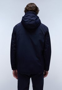 Marineblauwe waterdichte jas met een capuchon en elastische manchetten. Heeft een gladde textuur en een ontspannen pasvorm. Achteraan is er minimale detaillering.