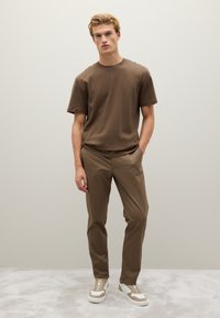 T-shirt di cotone marrone a maniche corte abbinato a pantaloni marroni su misura. Sneakers bianche e beige con lacci. Design minimalista, texture liscia.