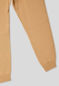 Pantaloni sportivi beige realizzati in materiale morbido, con un design affusolato, polsini elasticizzati e cuciture piatte per comfort.