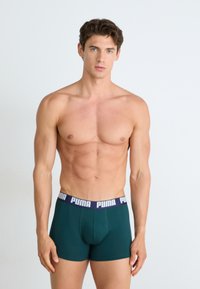 Boxer briefs verdes com uma cintura azul marinha que apresenta o logótipo branco "PUMA". Tecido suave, design ajustado e comprimento até à midida da coxa.