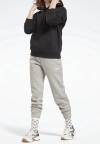 Felpa nera con tasca anteriore, pantaloni della tuta grigi con un logo bianco, scarpe bianche con accenti neri e calze con motivi a disegni neri.