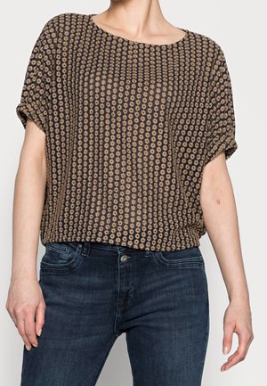 Brązowa krótka bluzka z krótkim rękawem ozdobiona kwiatowym wzorem z żółtymi akcentami, wykonana z lekkiego materiału, o luźnym kroju. Połączona z ciemnymi dżinsami.