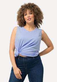 Top senza maniche di un blu chiaro con un dettaglio annodato in vita, abbinato a jeans a vita alta di un blu scuro. Tessuto morbido e vestibilità rilassata.