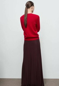 Czerwony sweter z dzianiny zestawiony z falującą burgundow�ą spódnicą, ukazując gładkie faktury i swobodny krój. Widok z tyłu podkreśla prostotę w projekcie.