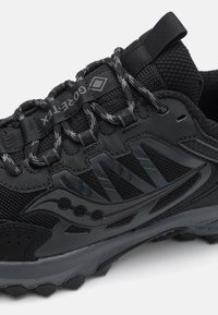 Czarny but treningowy z teksturowaną cholewą z tkaniny, plastikowymi akcentami i gumową podeszwą z bieżnikiem dla lepszej przyczepności.