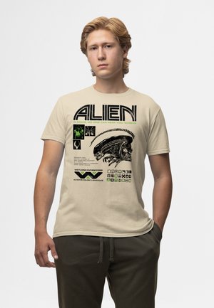 Beige Baumwoll-T-Shirt mit einem schwarzen Alien-Grafik und grünem Text mit Science-Fiction-Elementen, einschließlich Logos und Datenlayout.