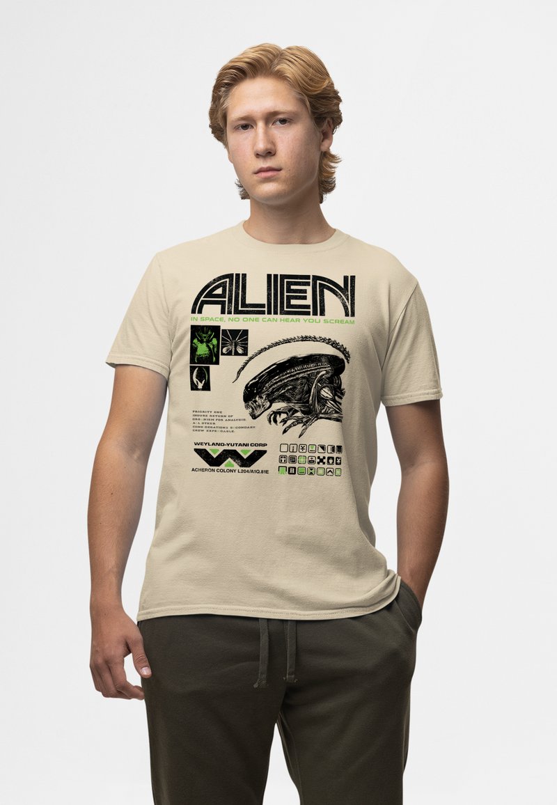 Camiseta de algodón beige con un gráfico negro de un extraterrestre y texto verde con elementos de ciencia ficción, incluyendo logotipos y formato de datos.