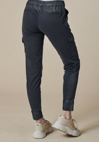 Schwarze Cargo-Hose mit elastischem Bund, schmaler Passform, Seitentaschen und gekrempelten Bündchen, kombiniert mit hellfarbenen Sportschuhen.