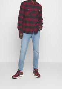 Röd- och svartrutigt skjorta med två bröstfickor, ljusblå slitna jeans och vinröda sneakers med vita detaljer.