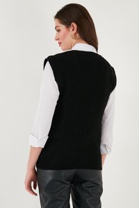 Musthave mustränihübe, millel on ribastruktuur ja varrukate puudumine; kantud valge särgi peale, koos mustade nahakujuliste pükstega.