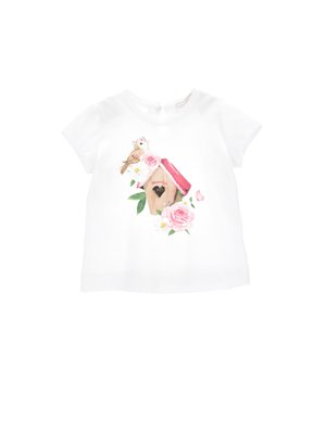 T-shirt bianco a maniche corte con un'illustrazione colorata di una casetta per uccelli con un uccello, rose e accenti floreali sul davanti.