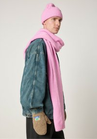 Roze gebreide muts en sjaal gecombineerd met een spijkerjack en bruine fleece wanten. De sjaal hangt losjes om de nek en voegt textuur toe.